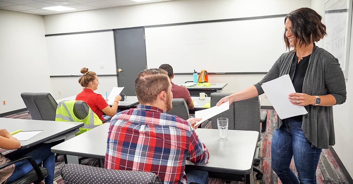 Instructor handing out training materials to participants in a classroom setting.