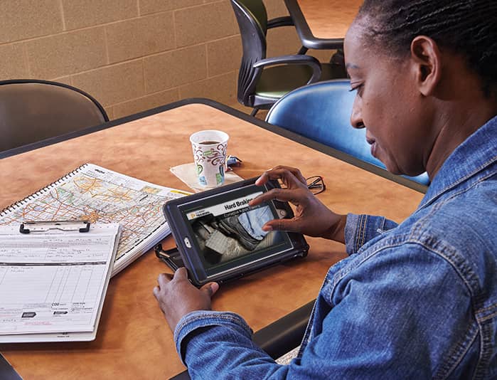 Driver uses tablet to complete online remedial training on hard braking, with safety materials on the table.