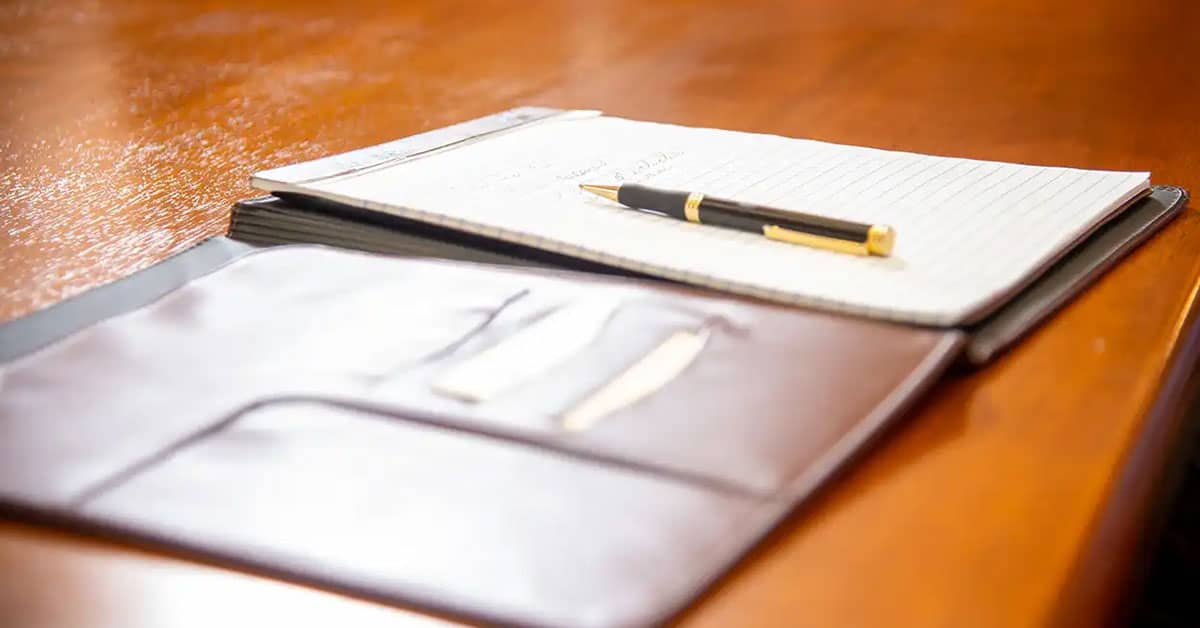 Training Program Planning Essentials Open leather folder with a notebook and pen on a wooden table, symbolizing preparation and planning for a professional training program.