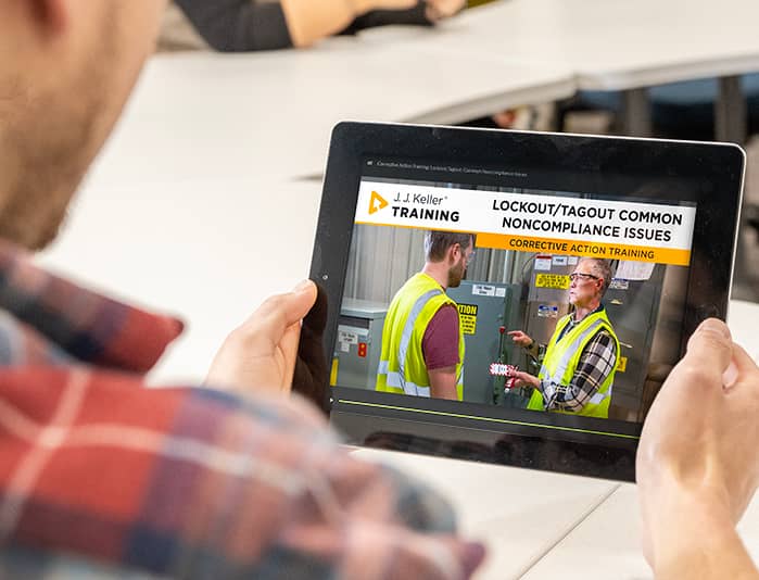 Employee viewing J. J. Keller corrective action training on lockout/tagout noncompliance issues, featuring workers in safety vests near industrial equipment.